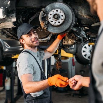 professional manual workers repairing car without wheel in mechanic shop